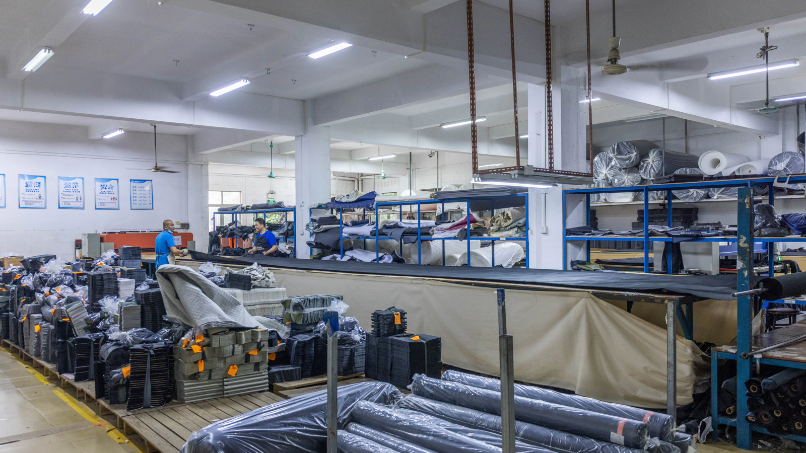 Factory material preparation area with textile rolls and stacks of cut bag panels