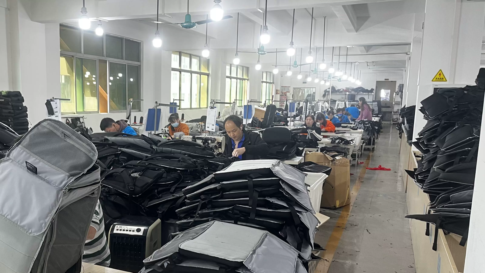 Bag sewing workshop with operators assembling backpack panels at industrial sewing stations