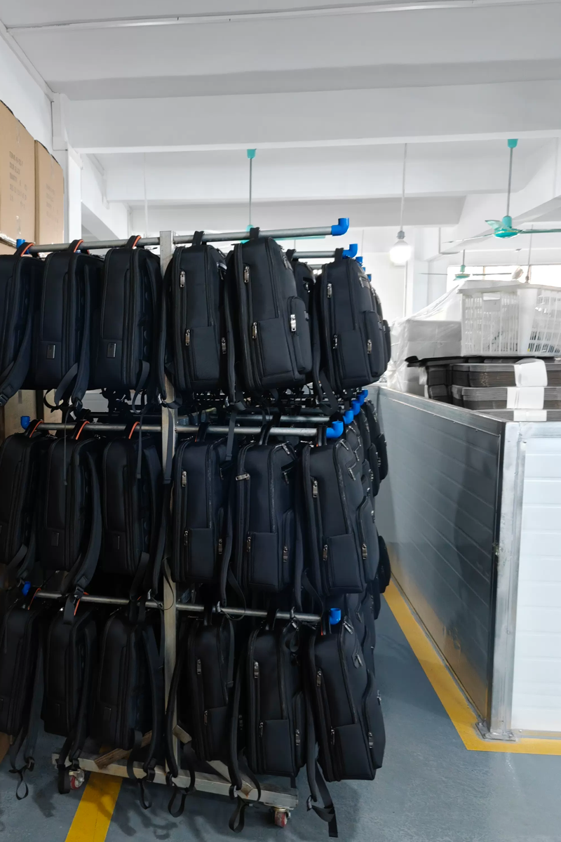 Rows of finished black backpacks arranged on a mobile rack beside packing cartons